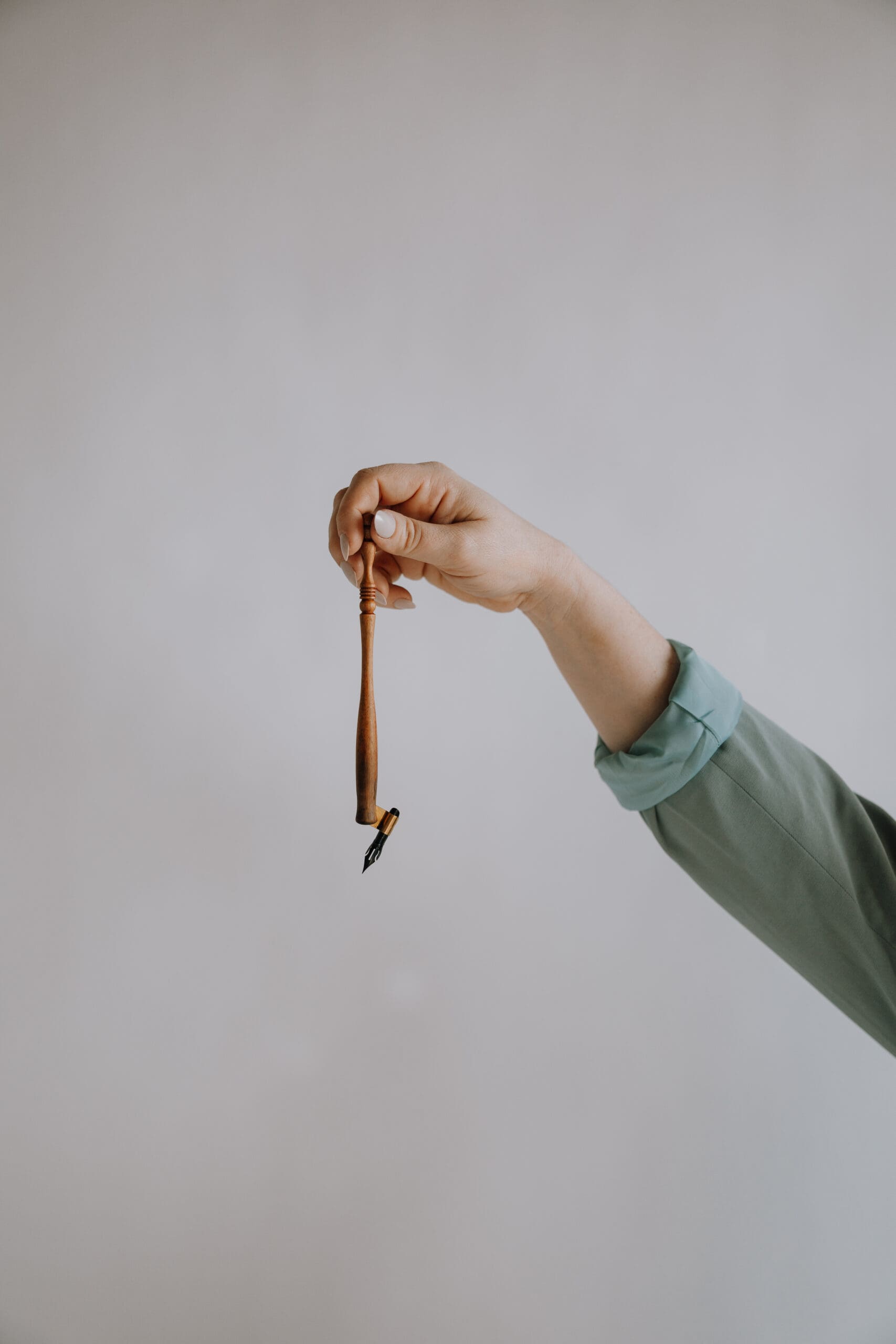 Hand Holding a Wood Oblique Calligraphy Pen in front of a cream colored background