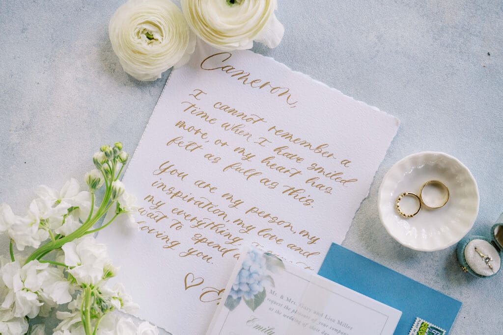 Image of calligraphy vows written on raw cotton paper decorated by florals and rings and ring dishes.