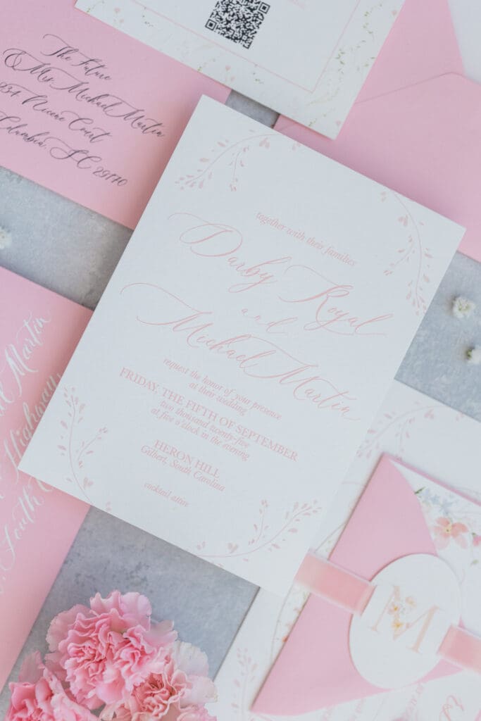 Styled flat lay of a pink wedding invitation suite with classic typography and soft pink details.